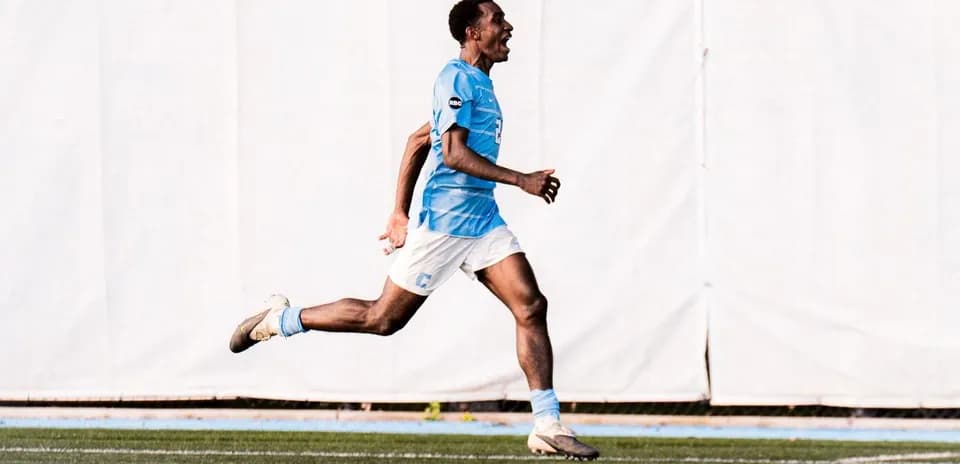 Jugador corriendo en campo de fútbol con camiseta azul
