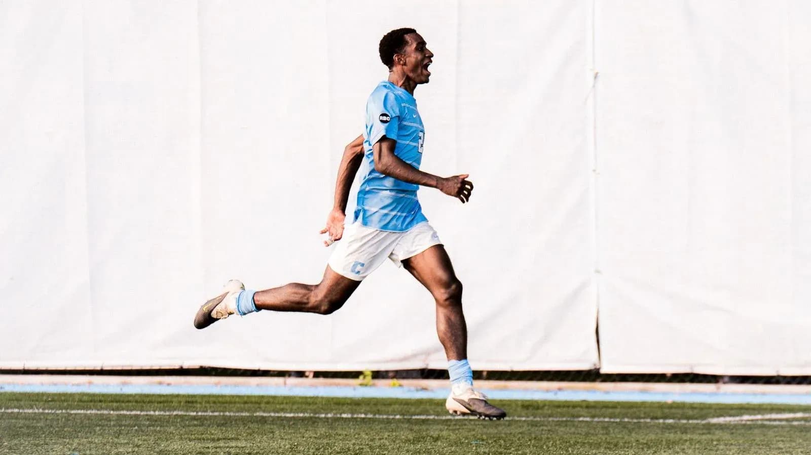 Jugador corriendo en campo de fútbol con camiseta azul