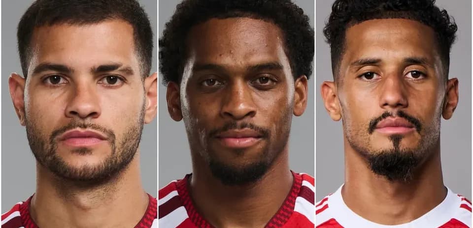 Tres jugadores posando con uniforme rojo en fondo gris