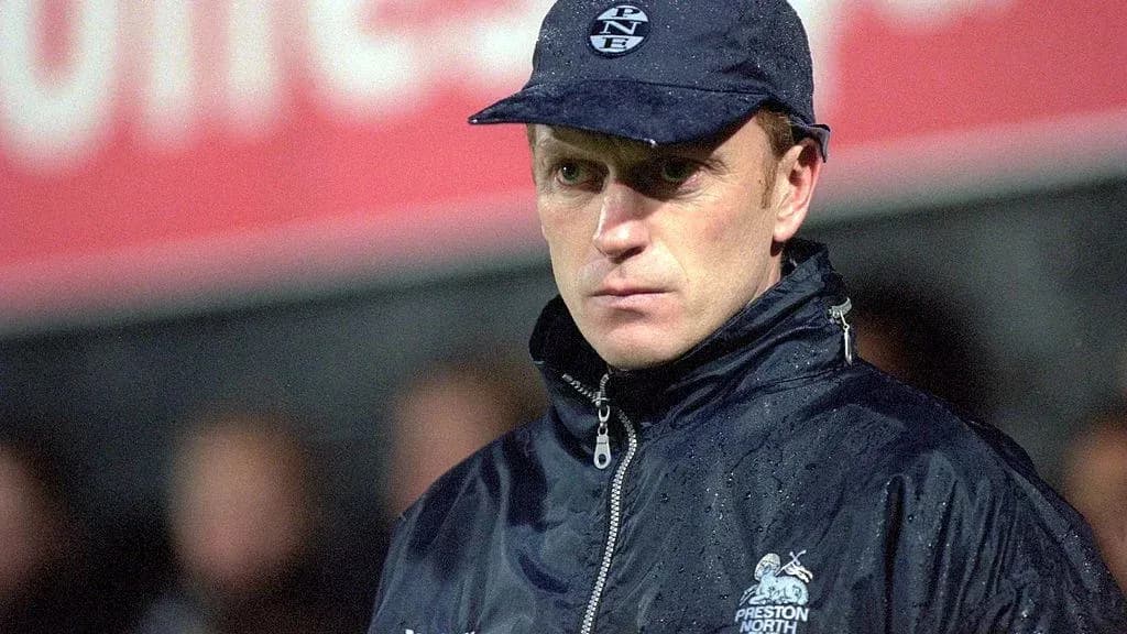 Entrenador de fútbol con chaqueta y gorra en campo