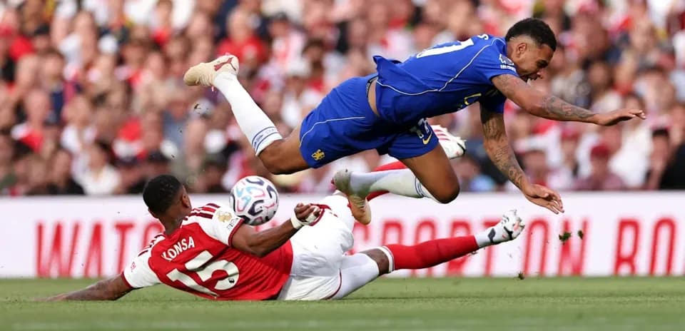 Jugador de Arsenal en el suelo, rival saltando sobre él