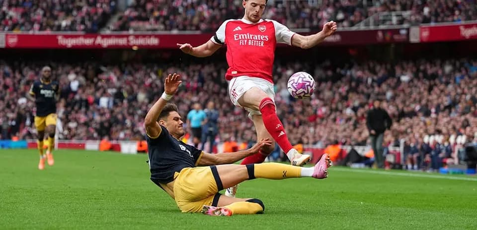 Jugador del Arsenal esquivando a un oponente caído