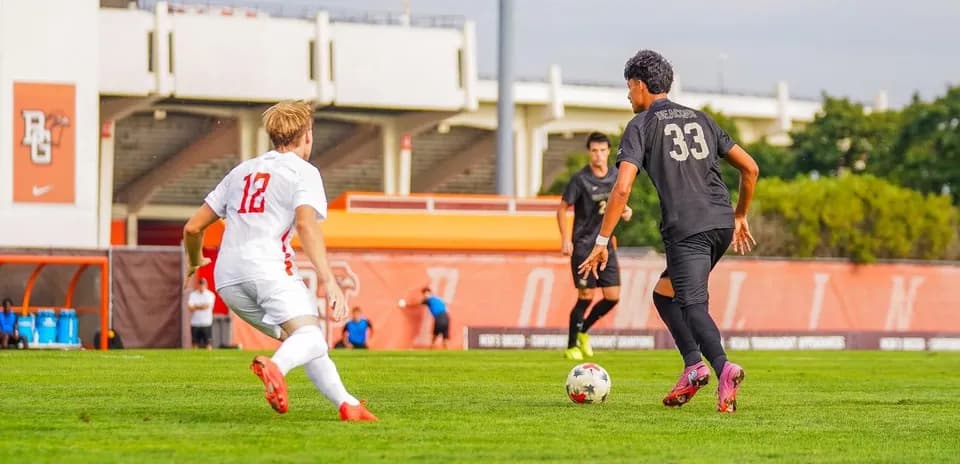Jugador en camiseta blanca persiguiendo balón hacia jugador negro