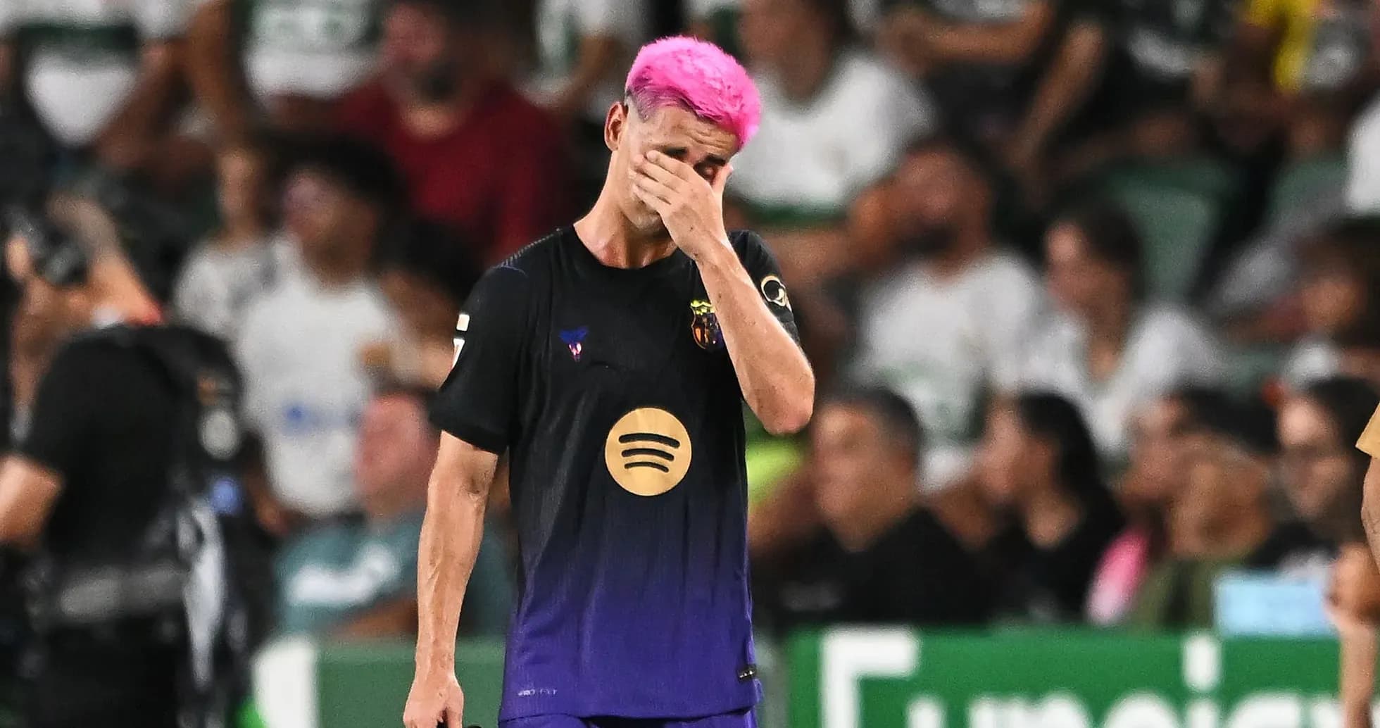 Jugador de fútbol con cabello rosa, cubriéndose la cara