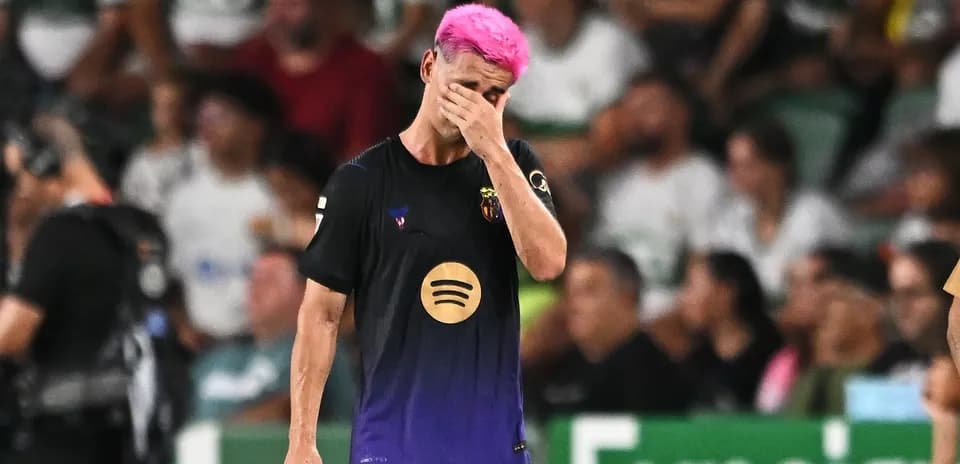 Jugador de fútbol con cabello rosa, cubriéndose la cara