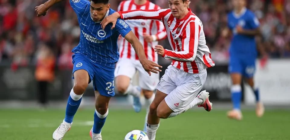 Jugador en camiseta azul y jugador en camiseta roja compiten por el balón