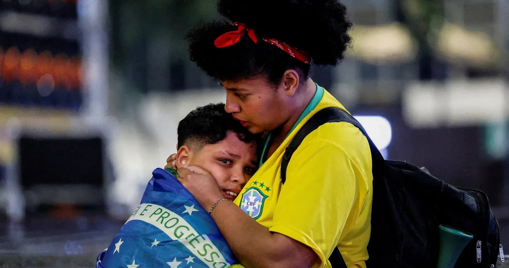 Mujer abrazando a niño envuelto en bandera brasileña