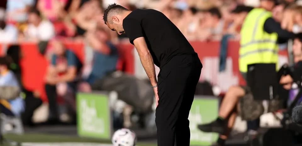 Entrenador agachado junto al balón en la línea de banda