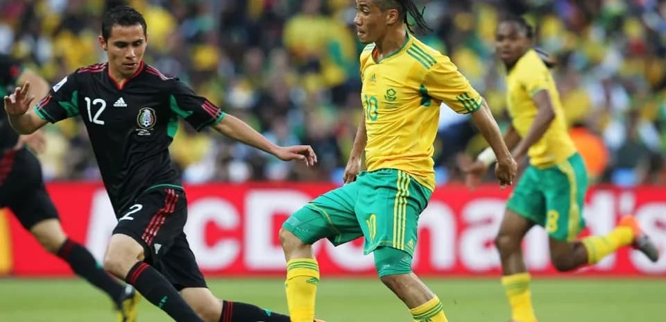 Jugador de Sudáfrica driblando a defensor mexicano
