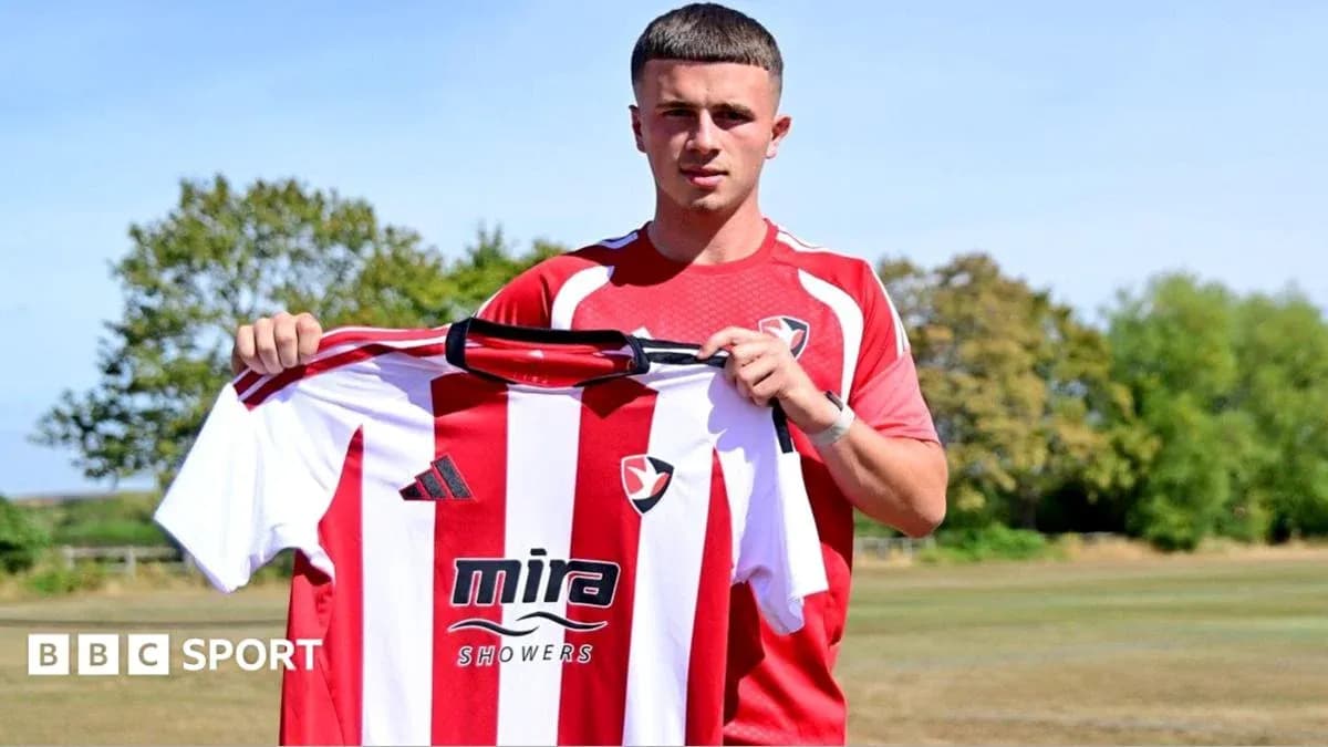 Jugador sosteniendo camiseta de Cheltenham Town en campo Jugador sosteniendo camiseta de Cheltenham Town en campo
