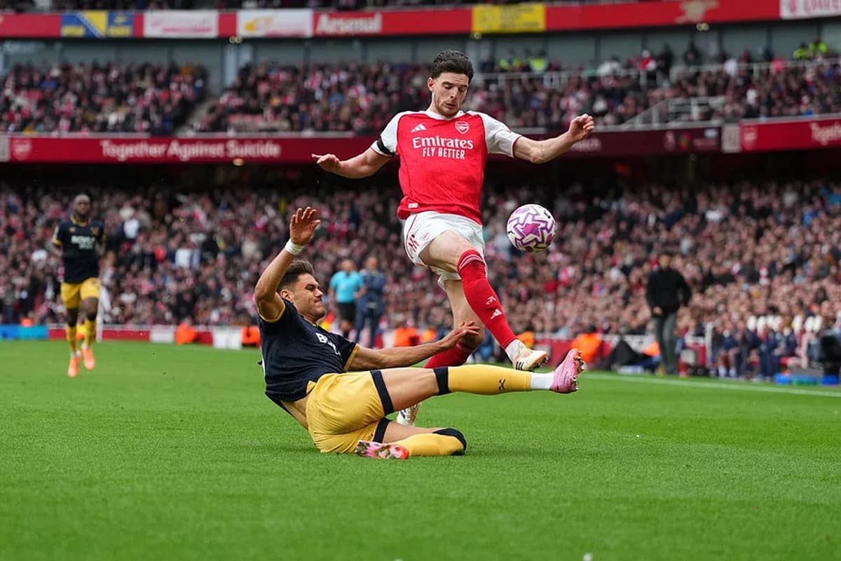 Jugador del Arsenal esquivando a un oponente caído Jugador del Arsenal esquivando a un oponente caído