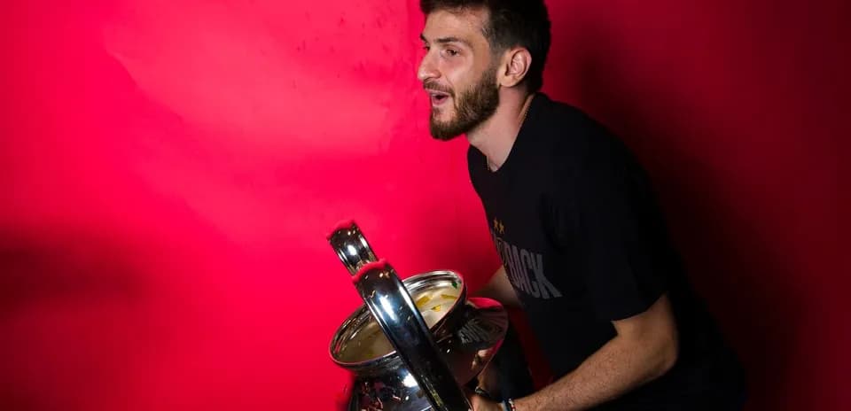 Jugador sosteniendo un trofeo frente a fondo rojo Jugador sosteniendo un trofeo frente a fondo rojo